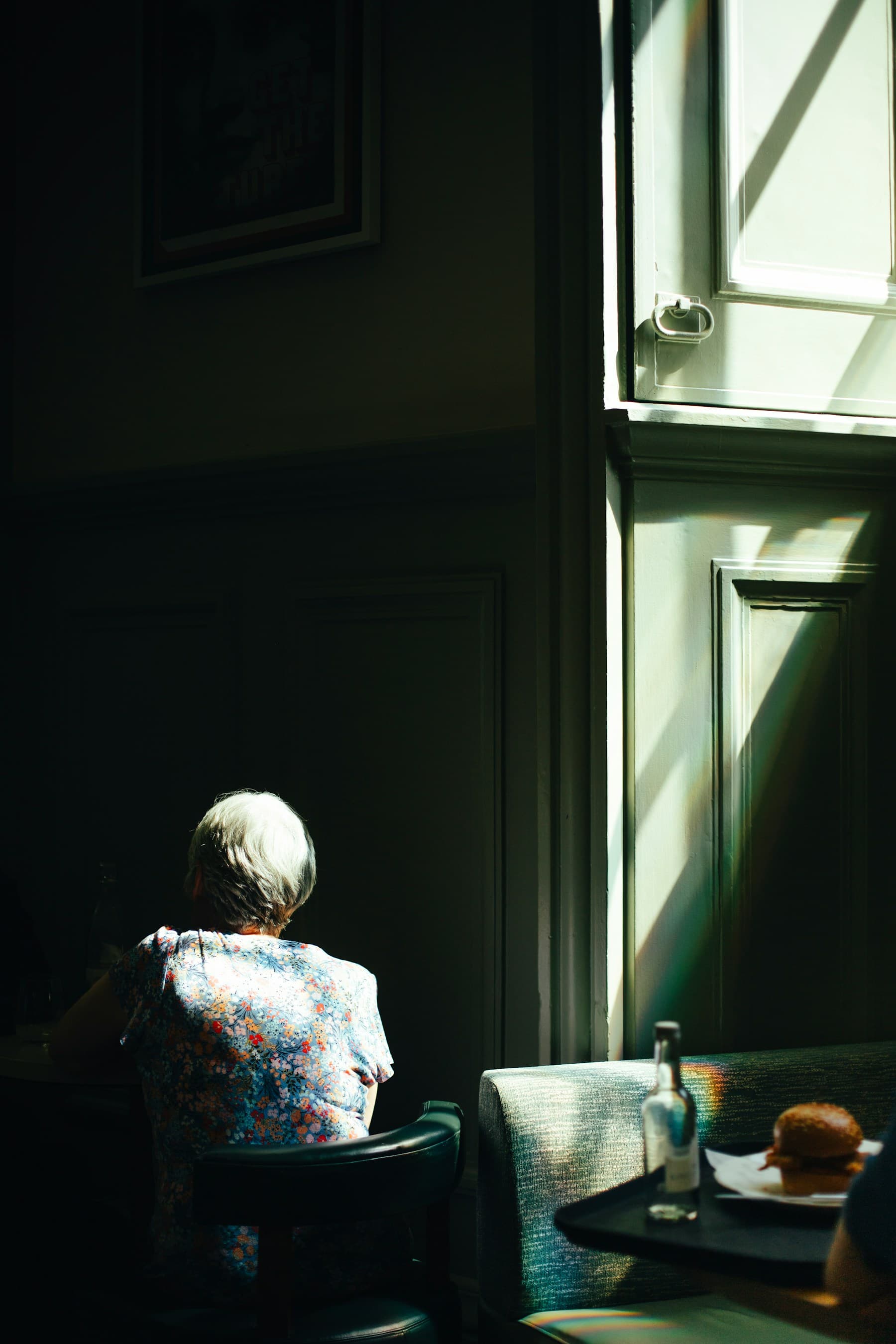 An older woman sitting quietly in sunlight beside a window at home