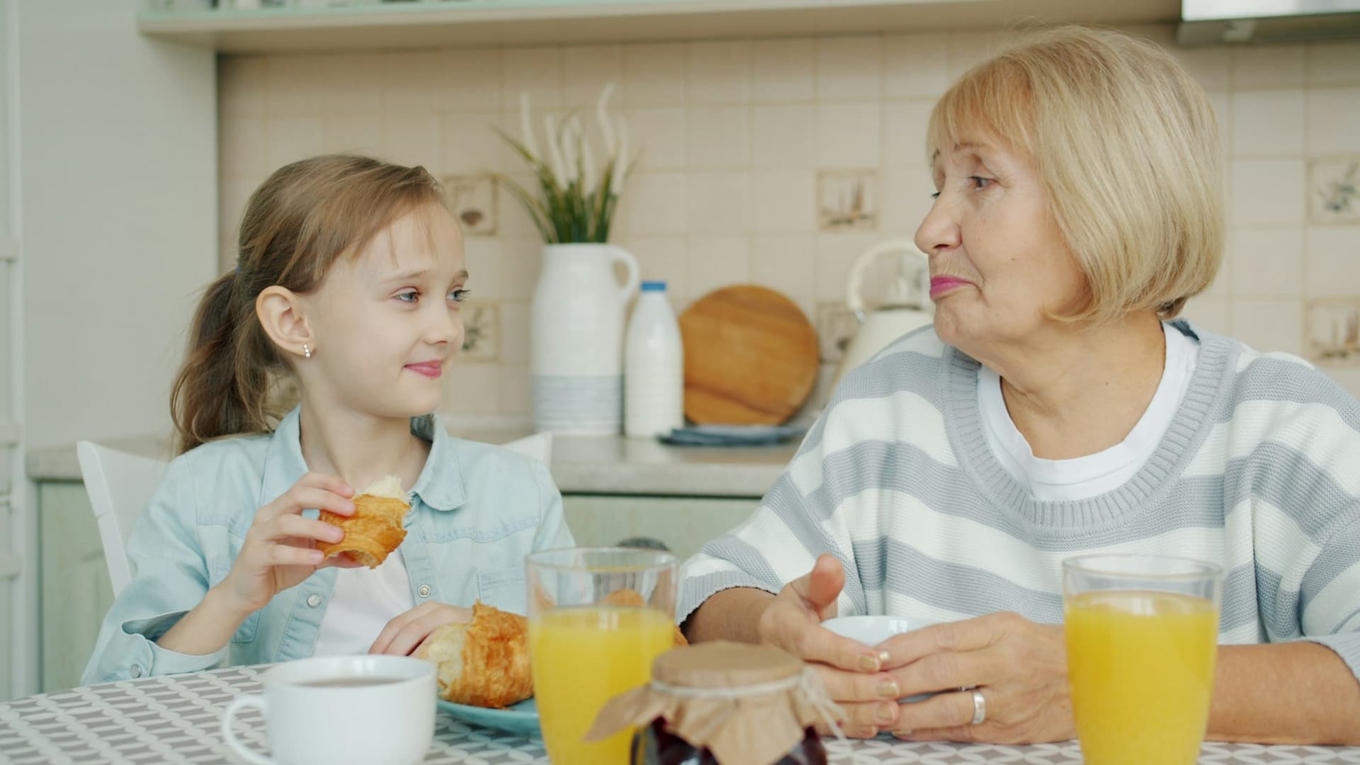 A grandmother and her granddaughter sharing breakfast and a laugh at the kitchen table