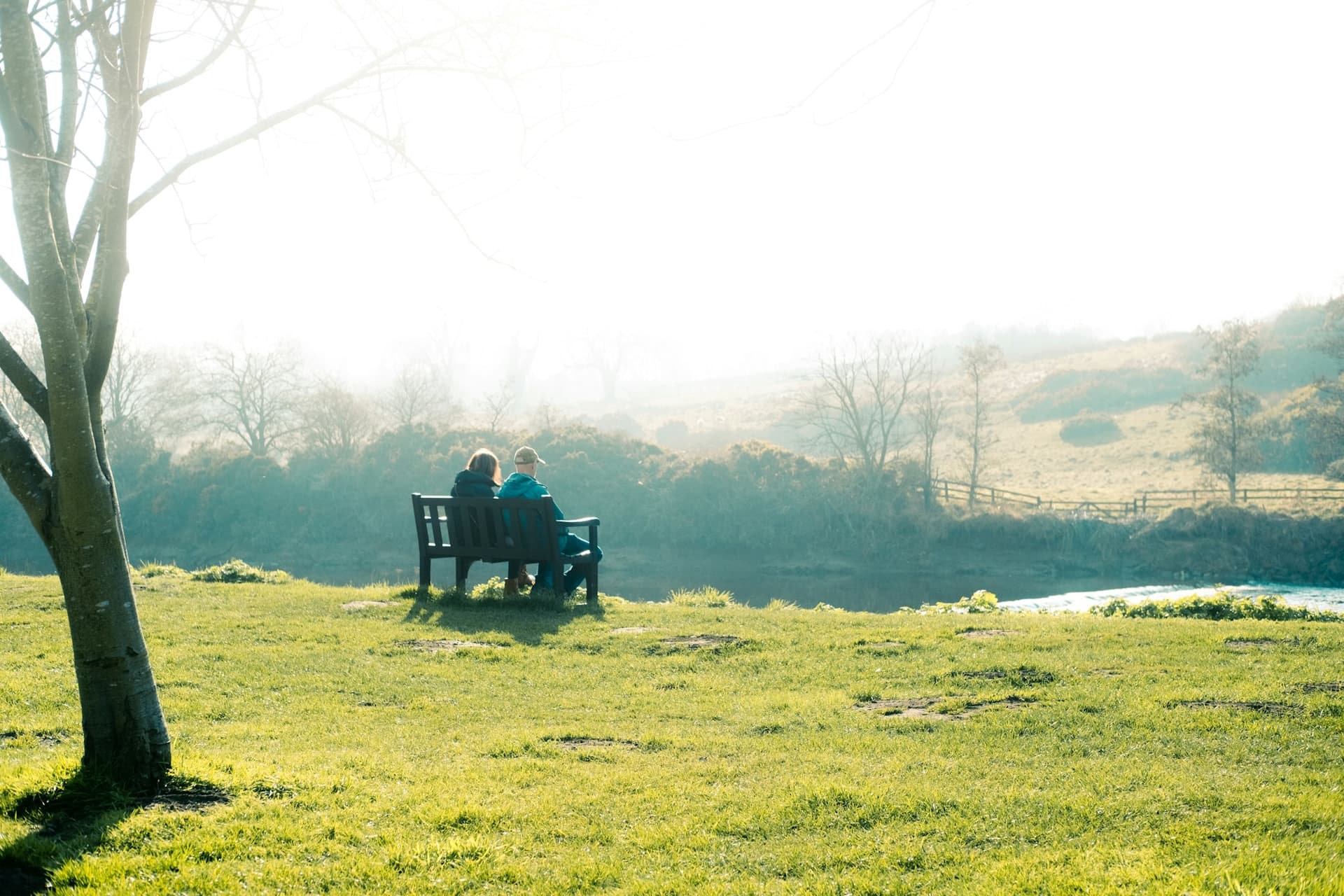 An older couple sitting together on a bench looking out over the countryside