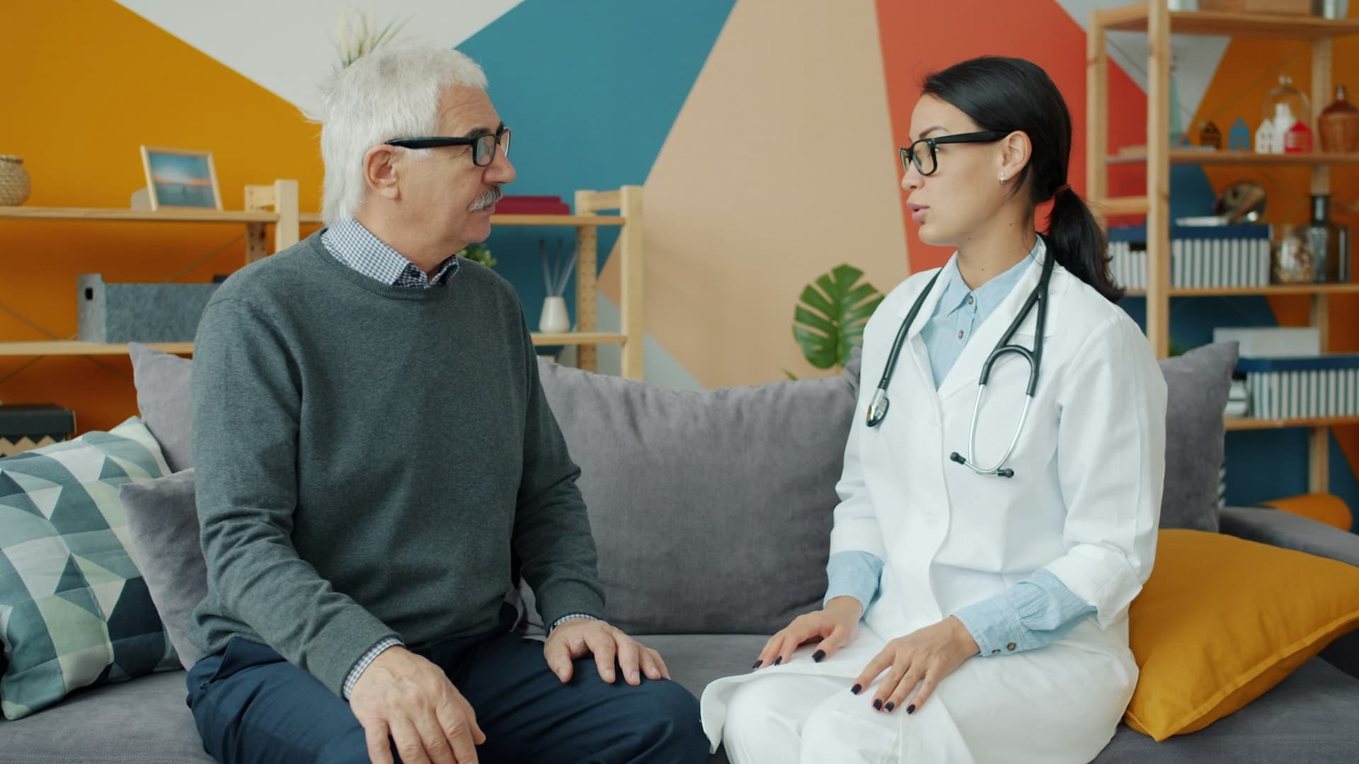 A health professional chatting with an older man on his sofa at home