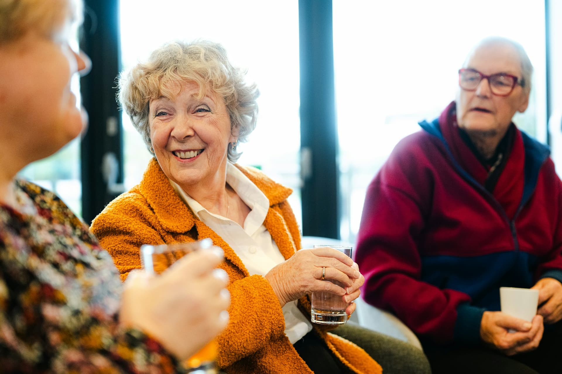 Three older friends laughing together over drinks in a bright café