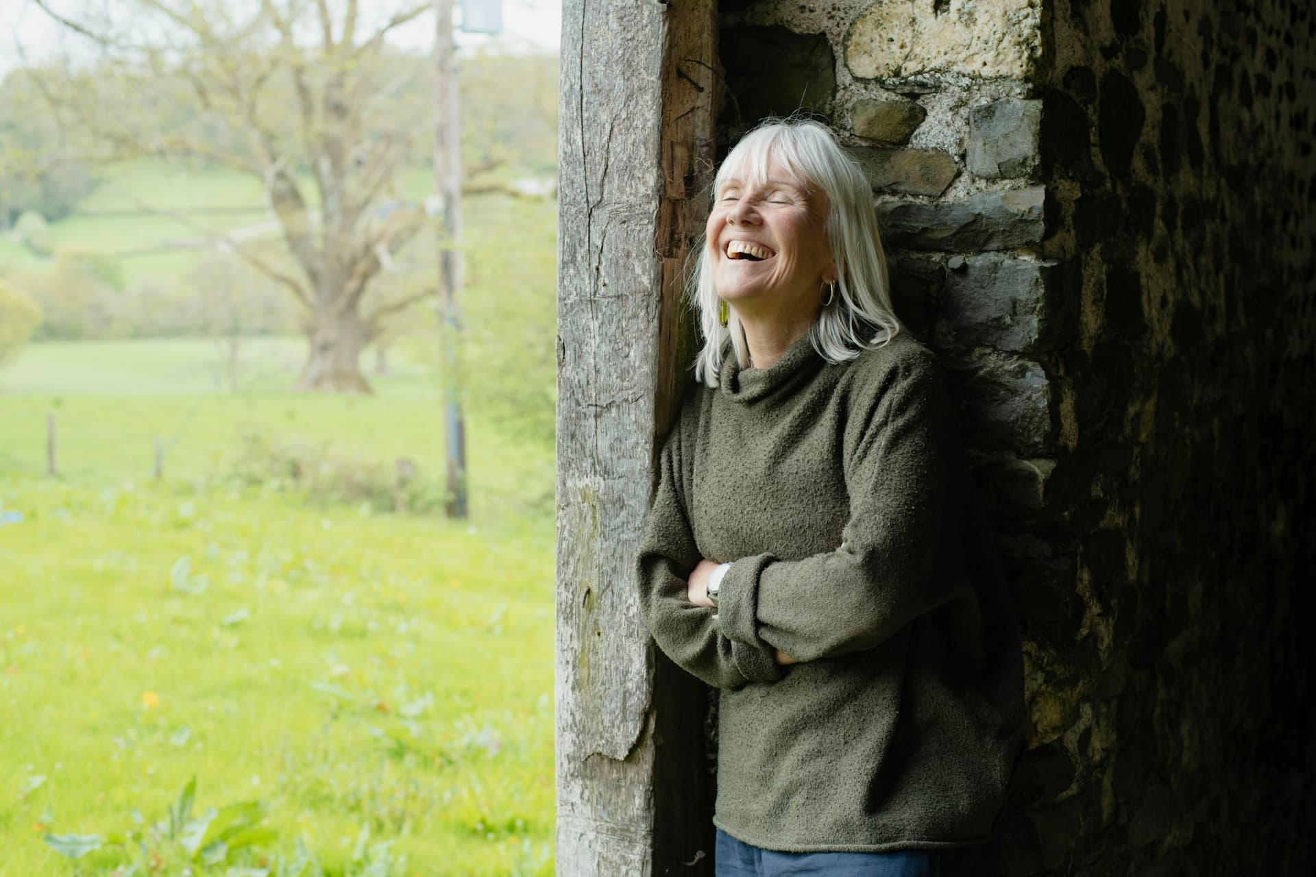An older woman laughing in a doorway overlooking a green field
