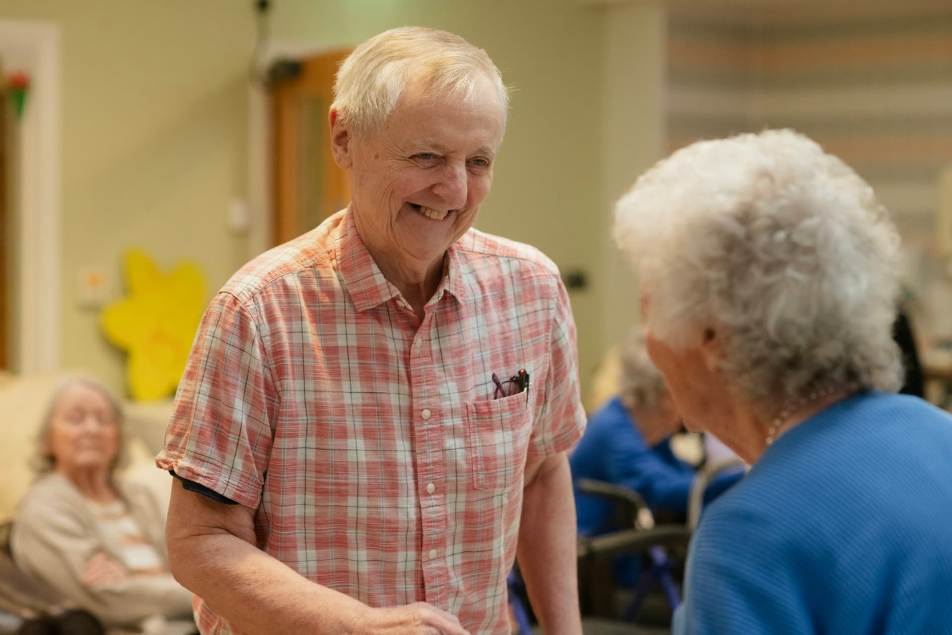 A volunteer greeting an older woman warmly in a community room